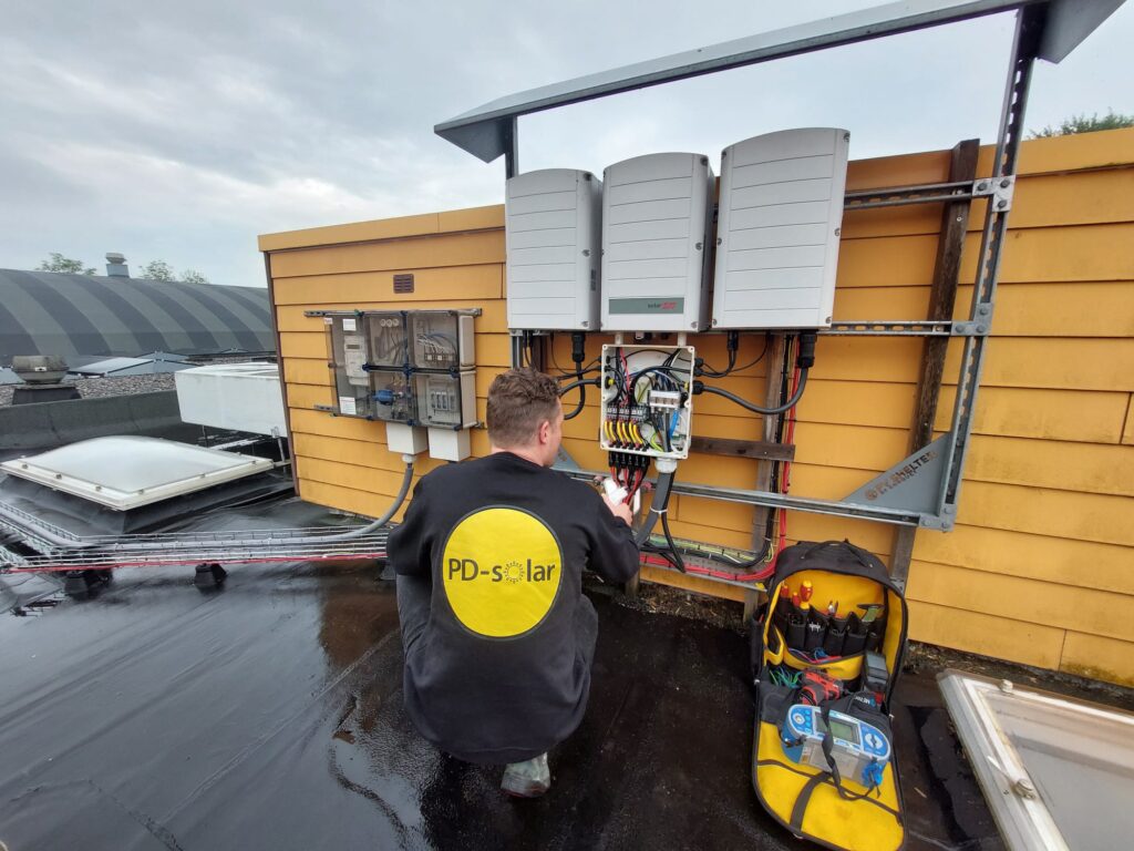 Monteur van PD-Solar sluit omvormers aan op een plat dak